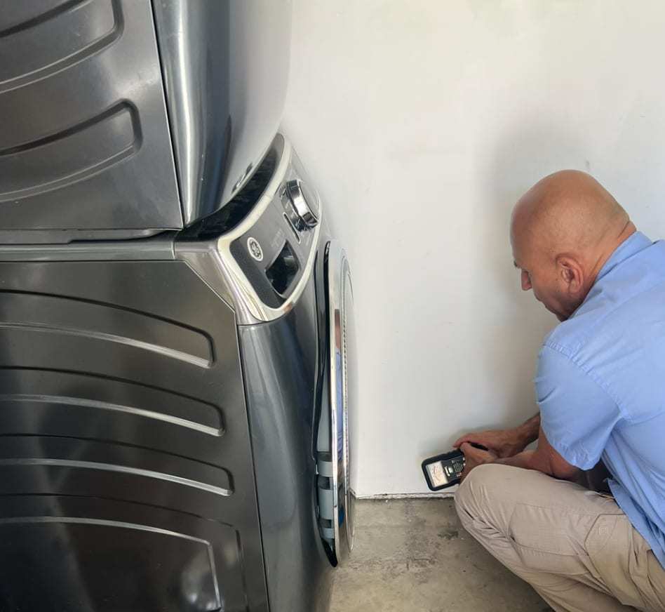 Inspector checking moisture at the base of a wall beside a washer