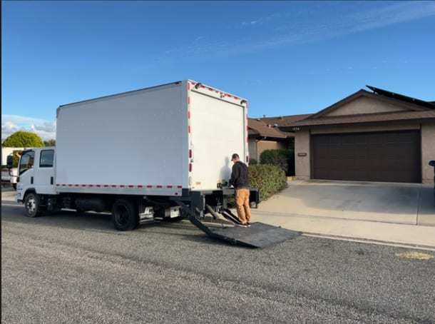 White box truck with its liftgate down in front of a house
