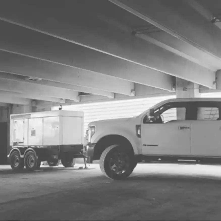 Pickup truck and an equipment trailer parked inside a garage, black and white