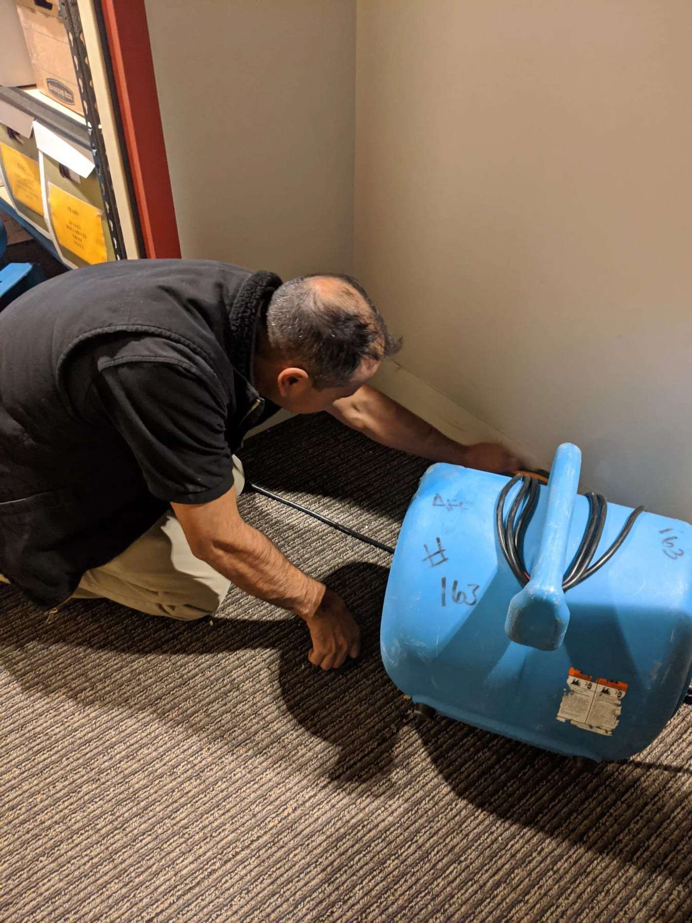 Technician kneeling to set an air mover at the edge of a wet carpet