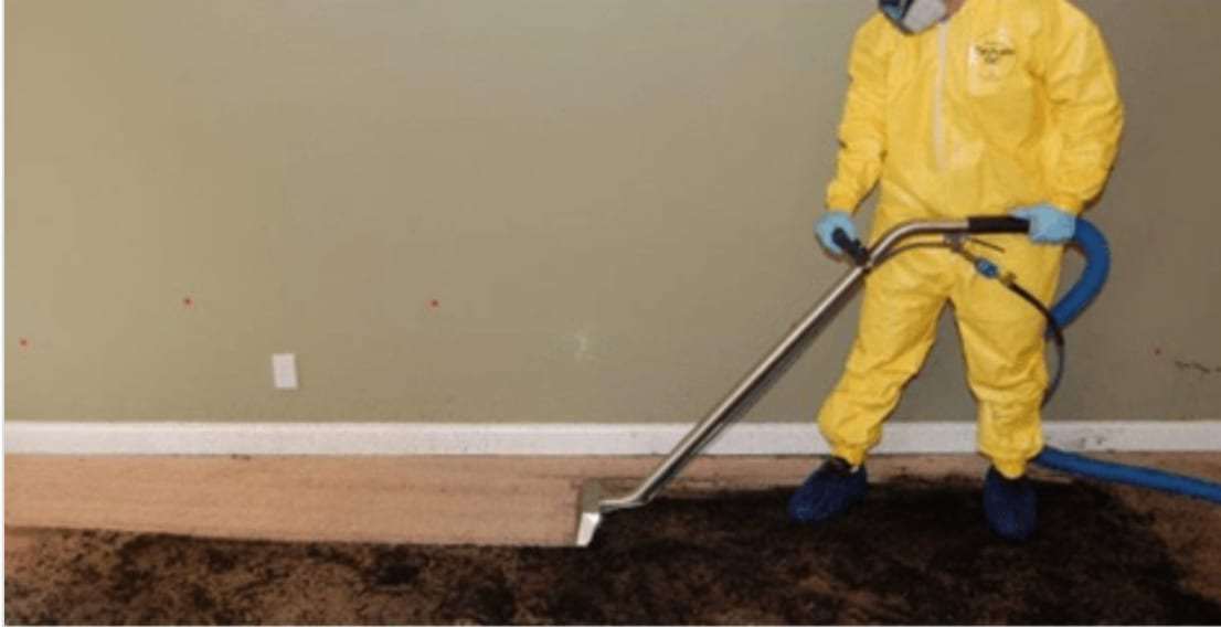 Technician in a protective suit extracting water from a soaked carpet