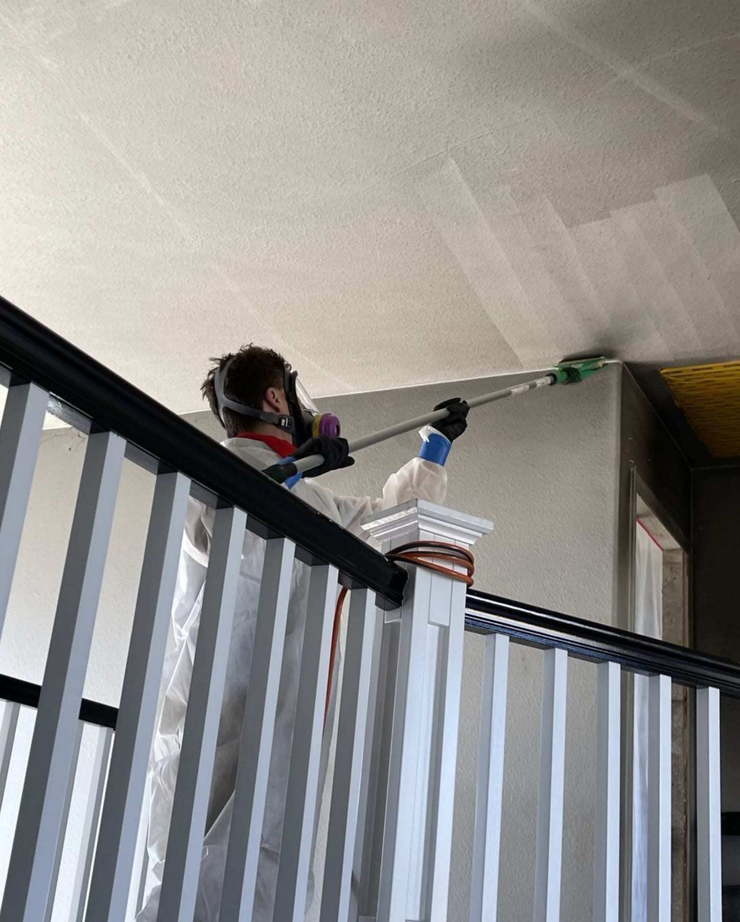 Technician in a respirator cleaning a high ceiling over a stair railing
