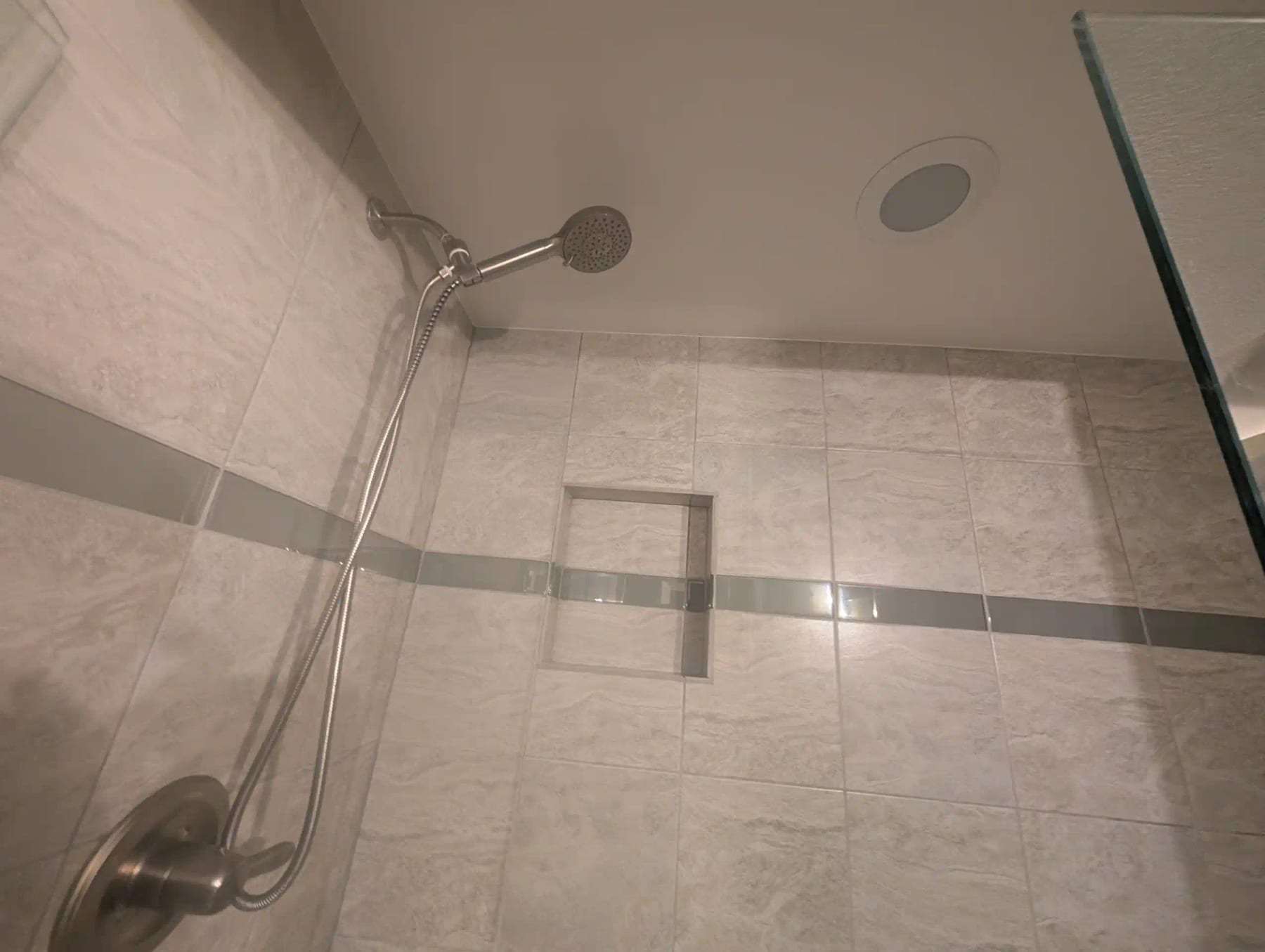 Tiled shower with a handheld shower head and a recessed niche