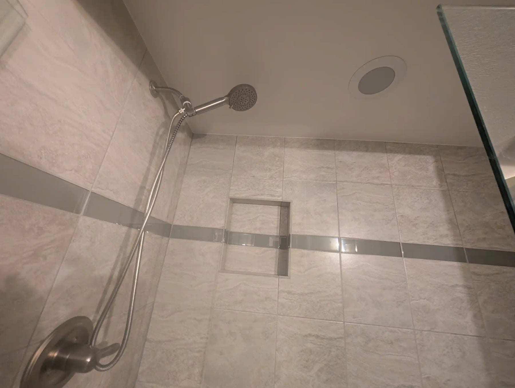 Tiled shower with a handheld shower head and a recessed niche