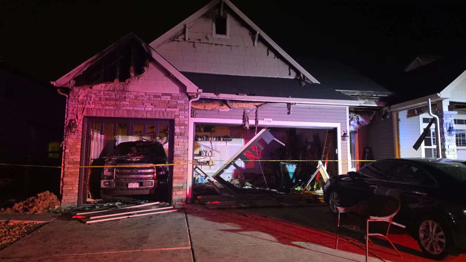 House with a fire-damaged garage and a burned vehicle at night
