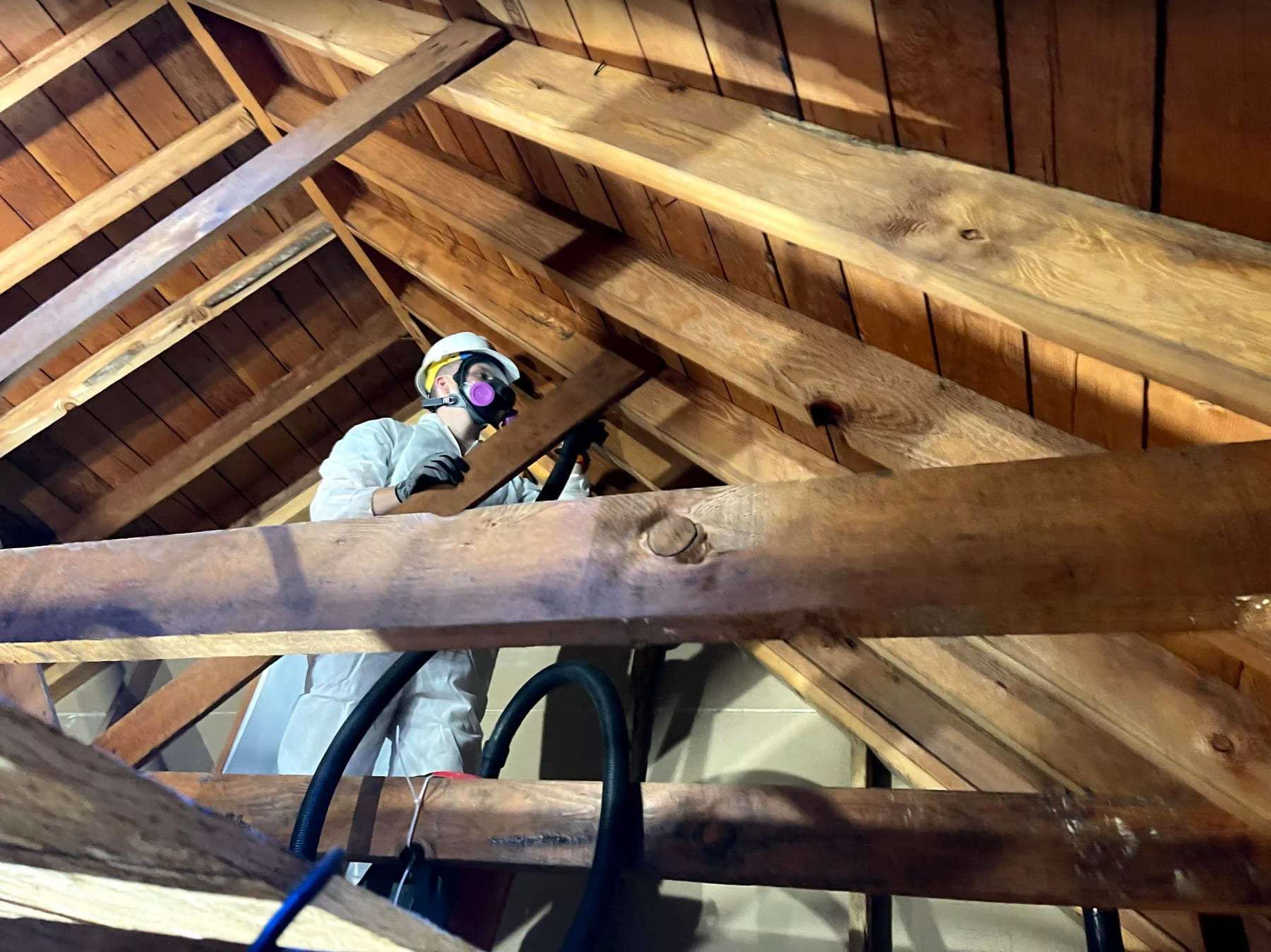 Technician in a respirator working among the rafters of an attic