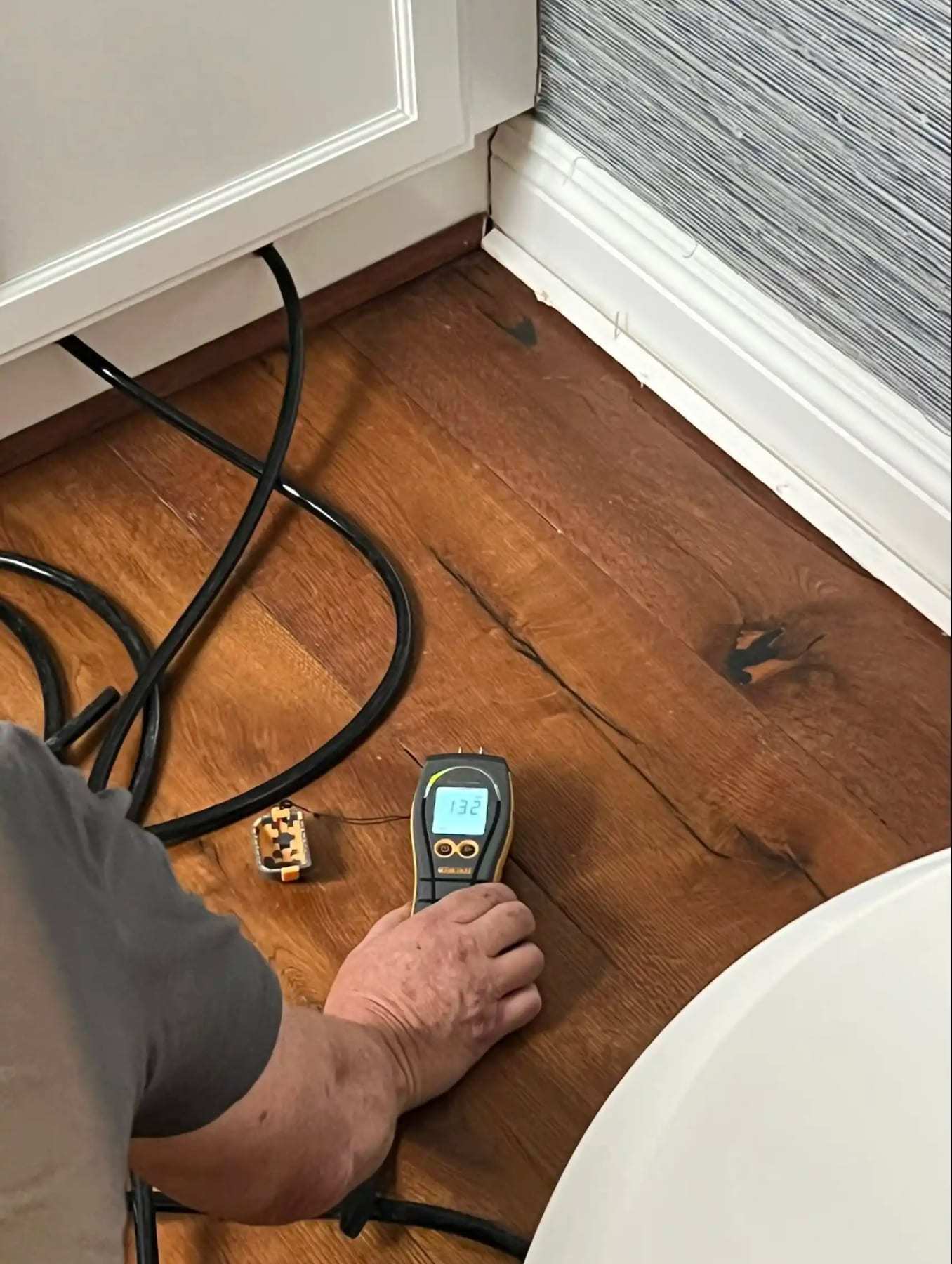 Hand holding a moisture meter on a hardwood floor