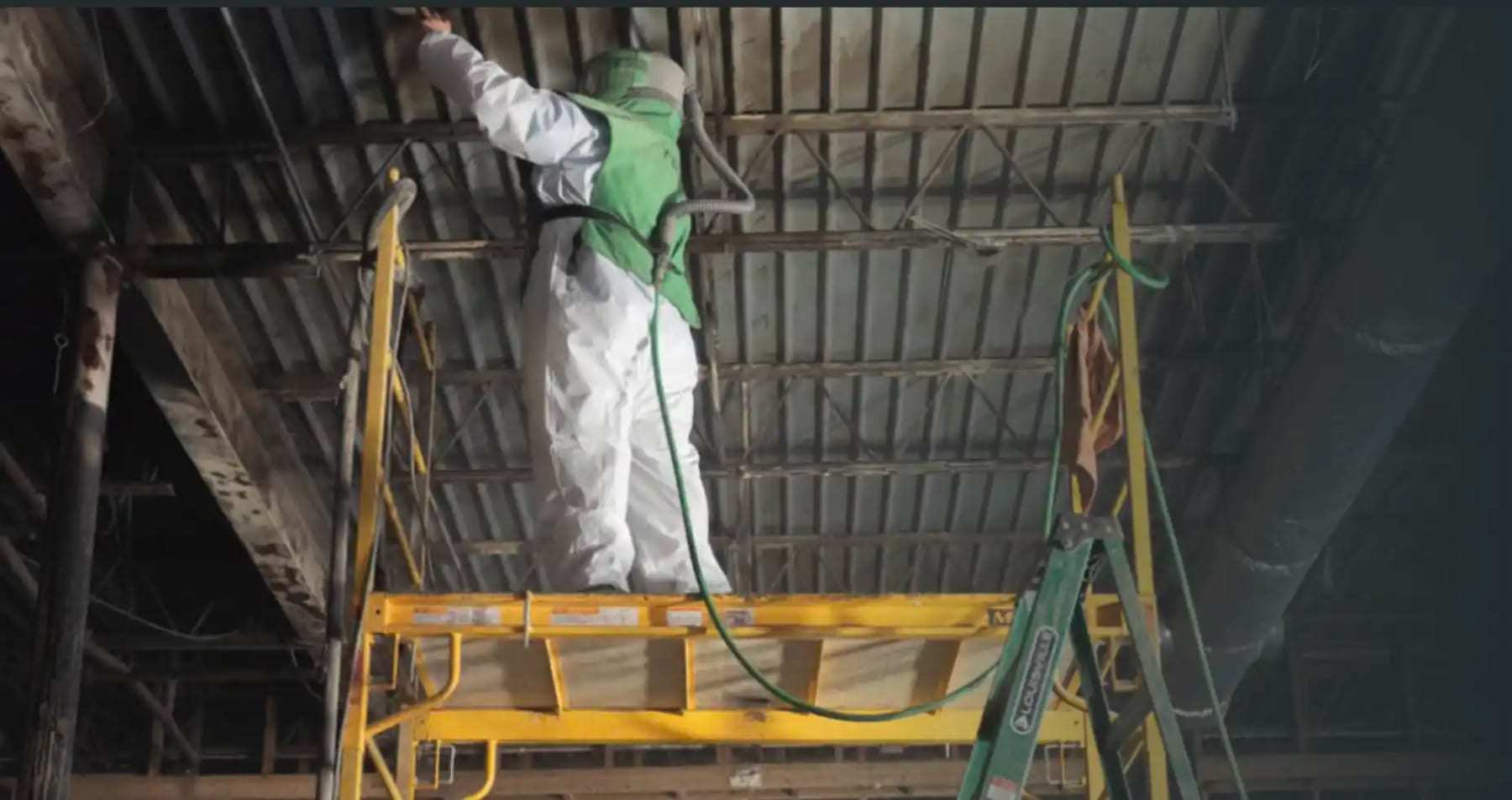 Technician on a ladder spraying the underside of a warehouse roof deck