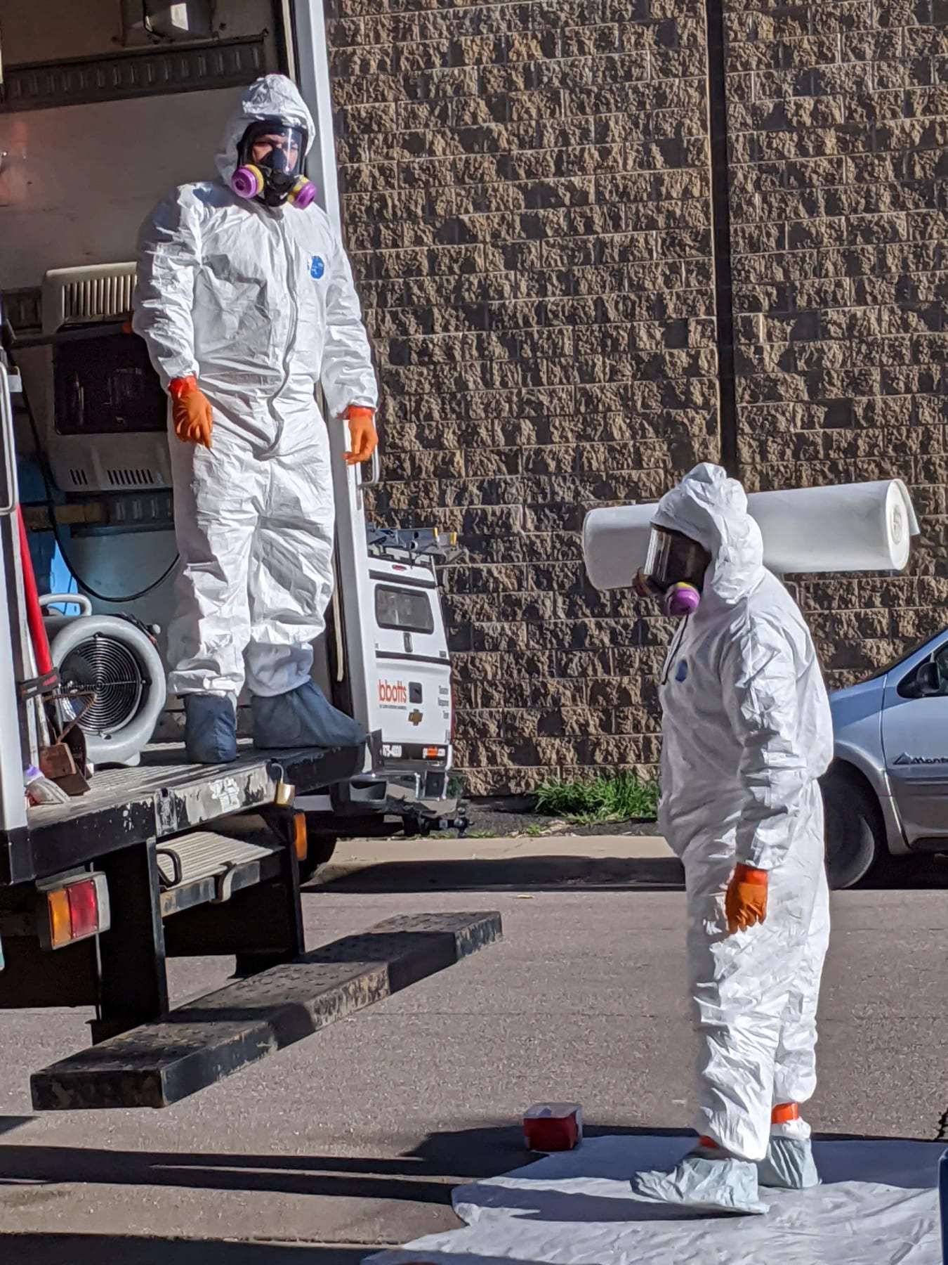 Two technicians in protective suits and respirators at the back of a service truck