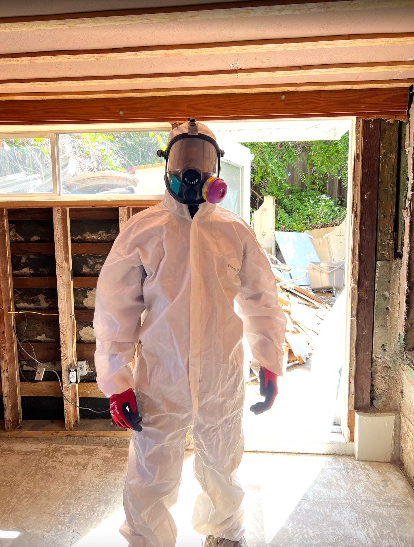 Worker in a protective suit and respirator in a gutted room