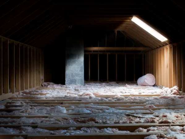 Dark attic with loose insulation between the floor joists