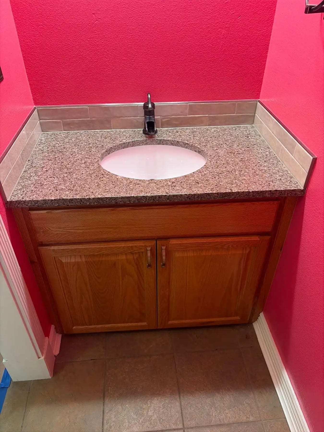 Bathroom vanity with an oak cabinet and granite top against a pink wall