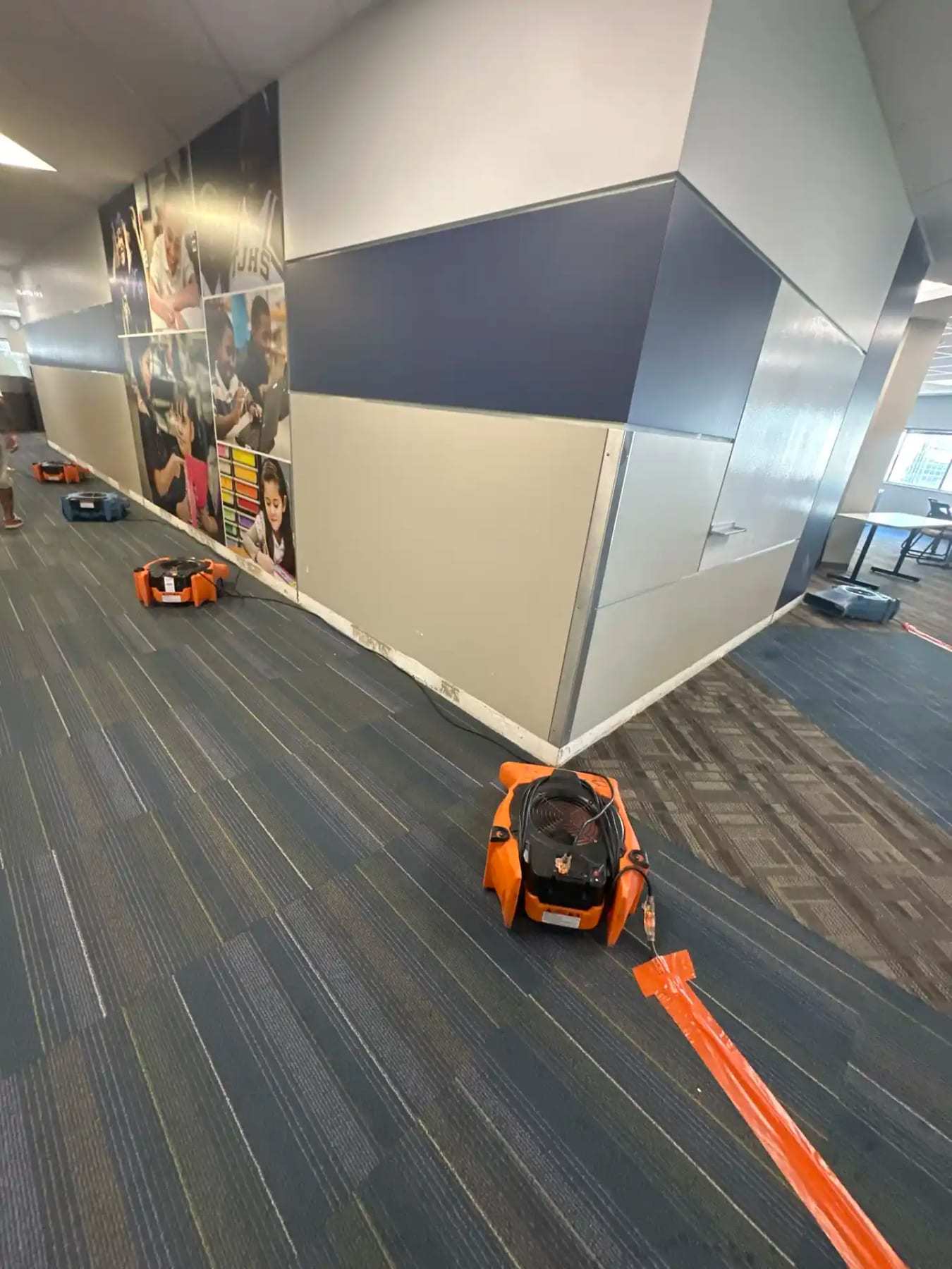 Air movers drying patterned carpet along an office corridor