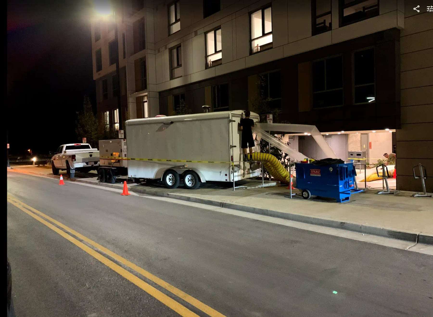 Equipment trailer and work truck parked at night outside a multi-story building