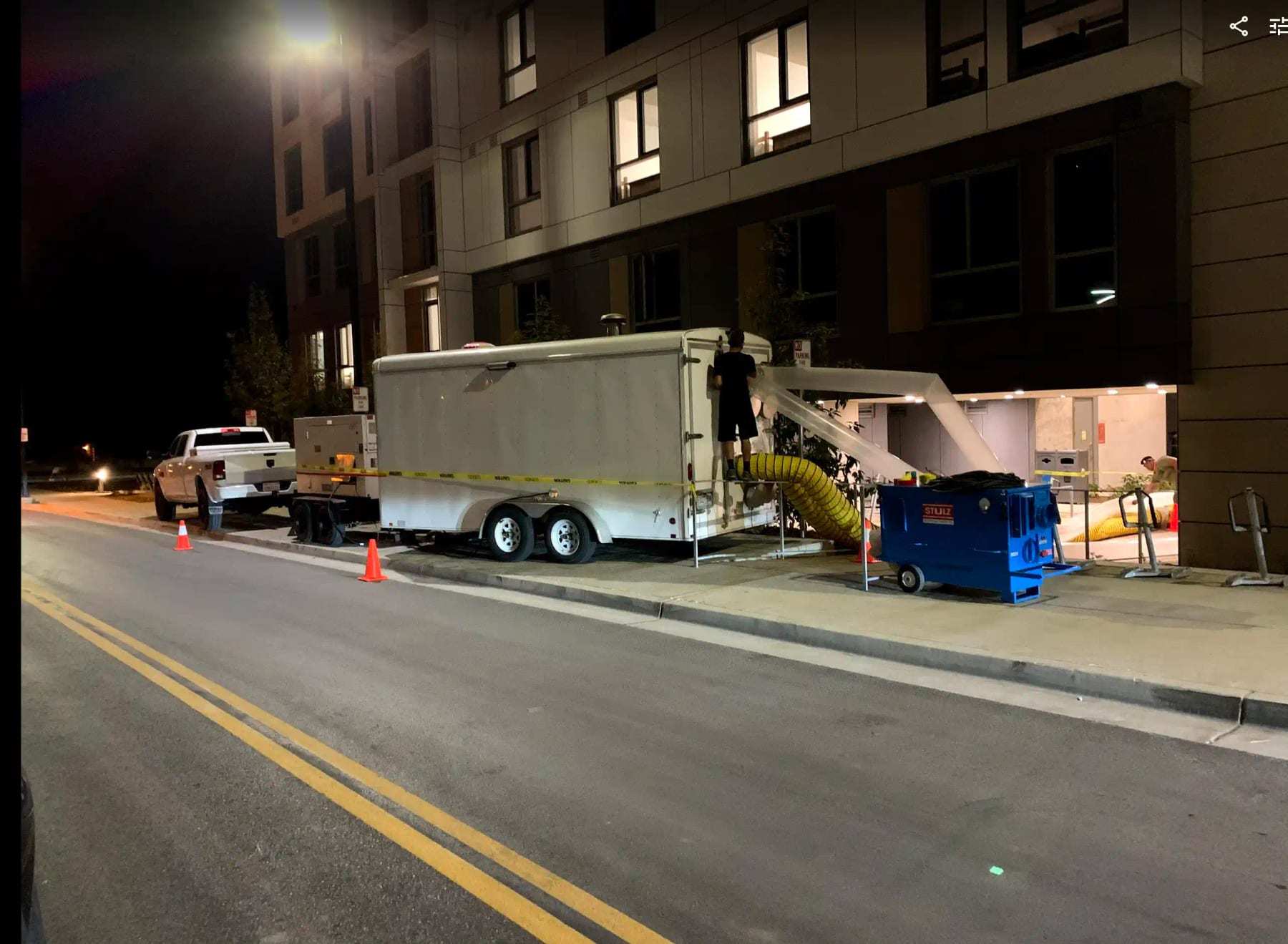 Equipment trailer and work truck parked at night outside a multi-story building