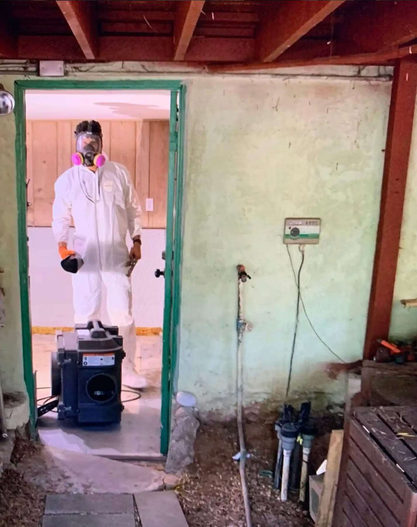 Technician in a protective suit at a basement doorway beside an air scrubber