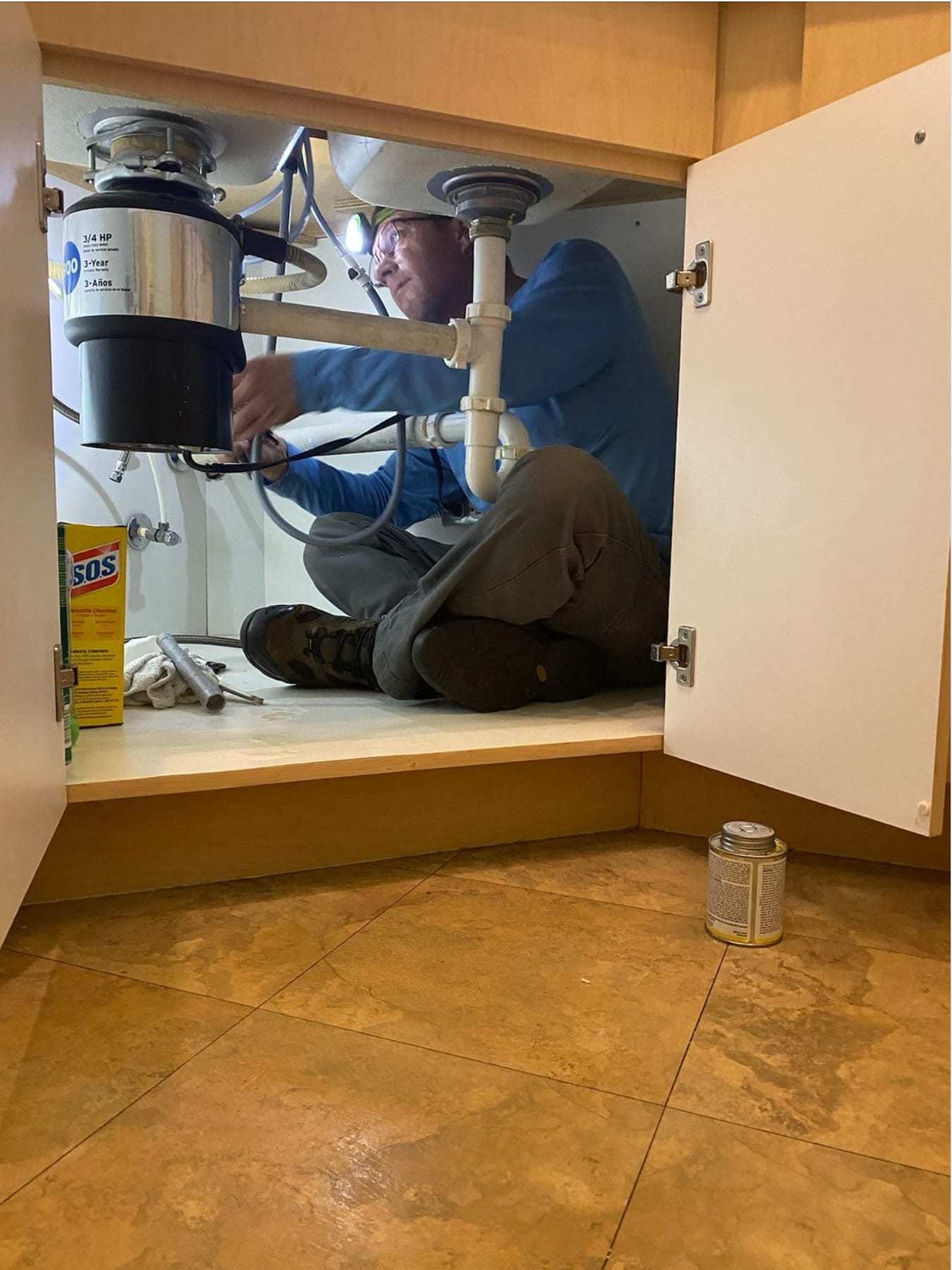 Plumber working under a kitchen sink on the supply lines and drain