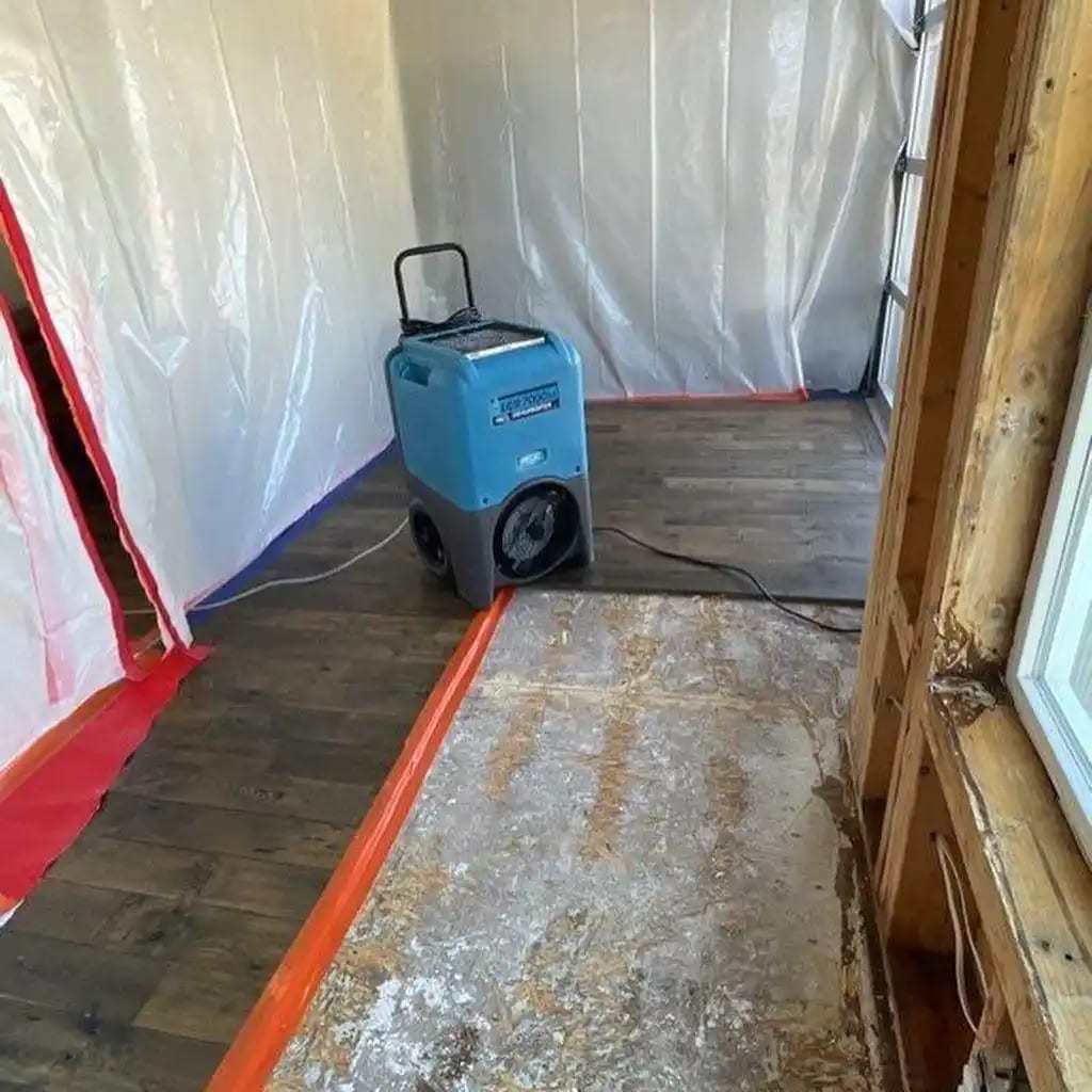 Dehumidifier running inside a plastic containment with the flooring removed