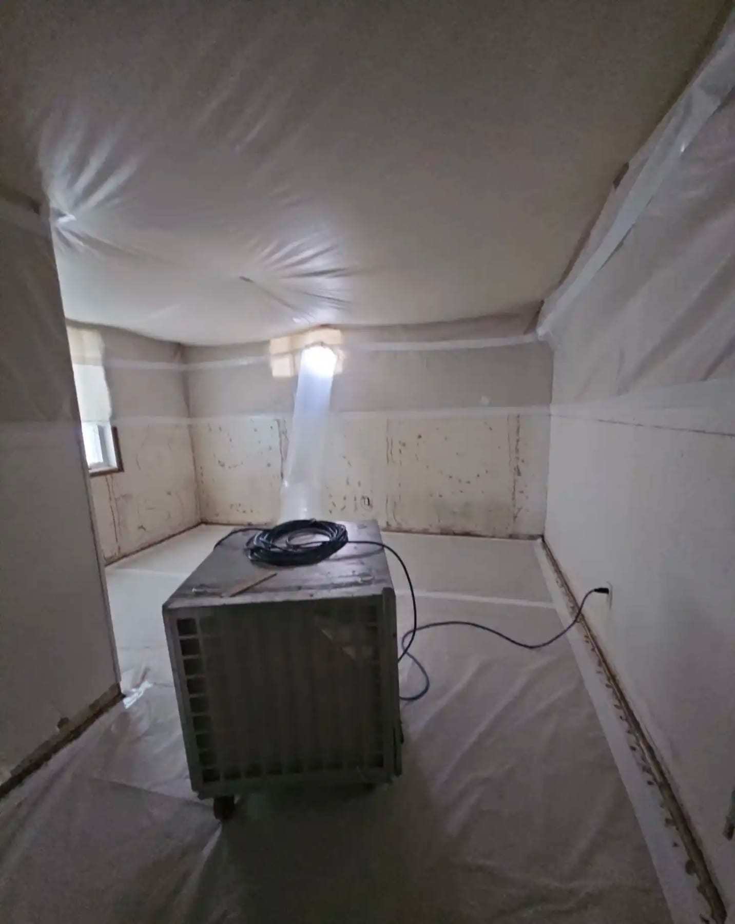 Room fully sheeted in plastic containment with a dehumidifier in the corner