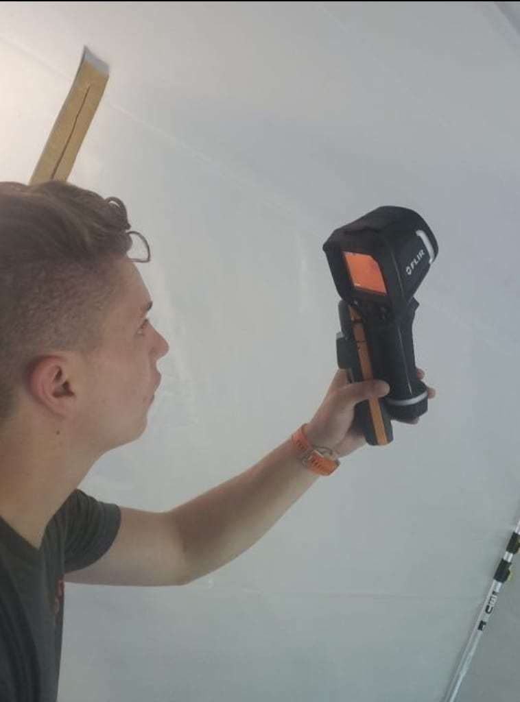 Technician scanning a plastic-covered wall with a thermal camera