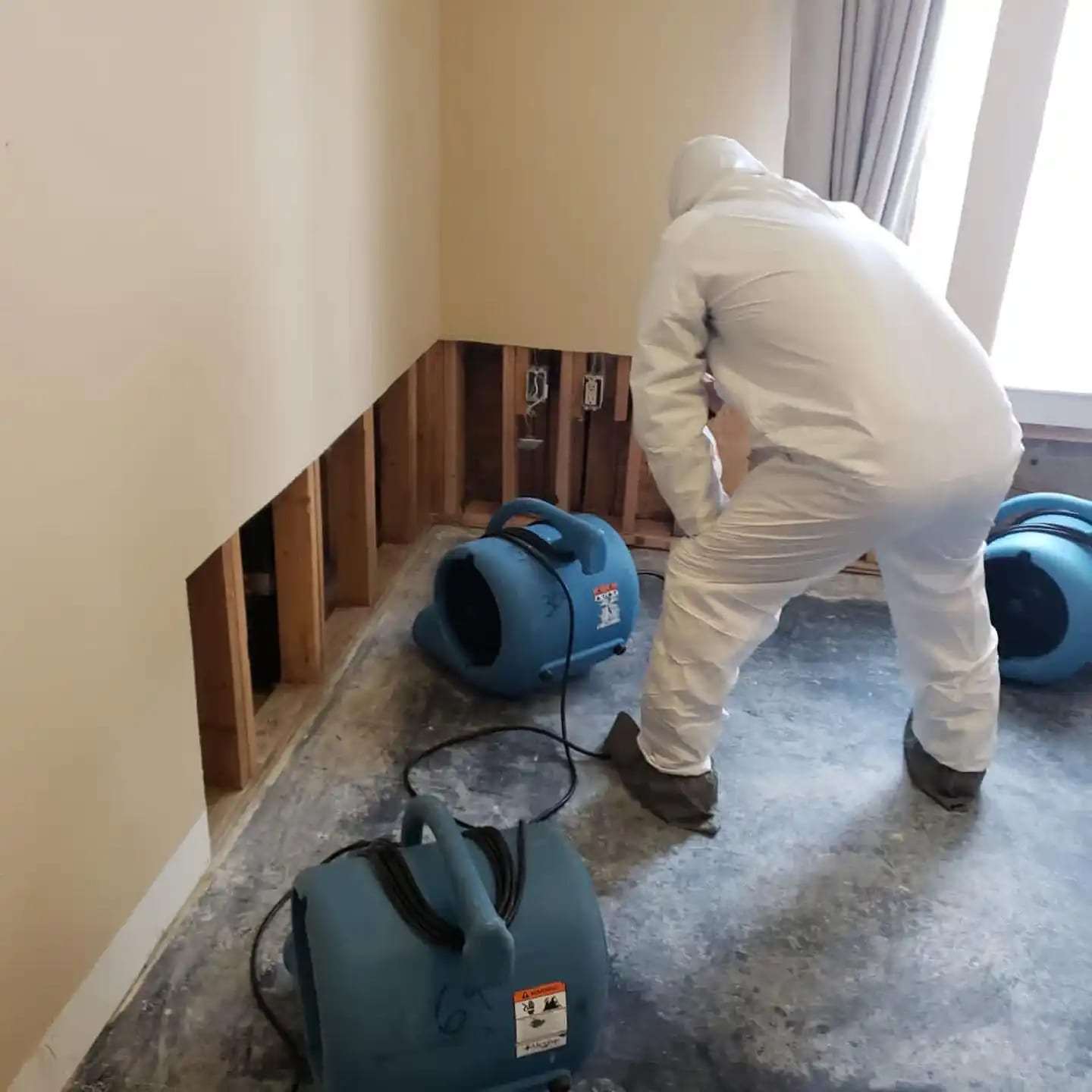 Technician in a protective suit in a flood-cut room with air movers running