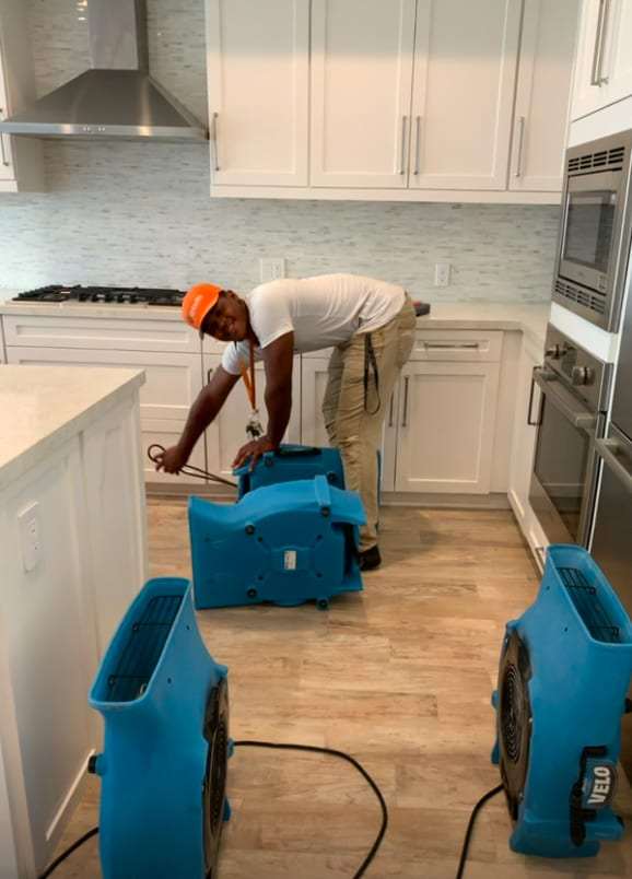 Technician placing air movers in a kitchen after a leak