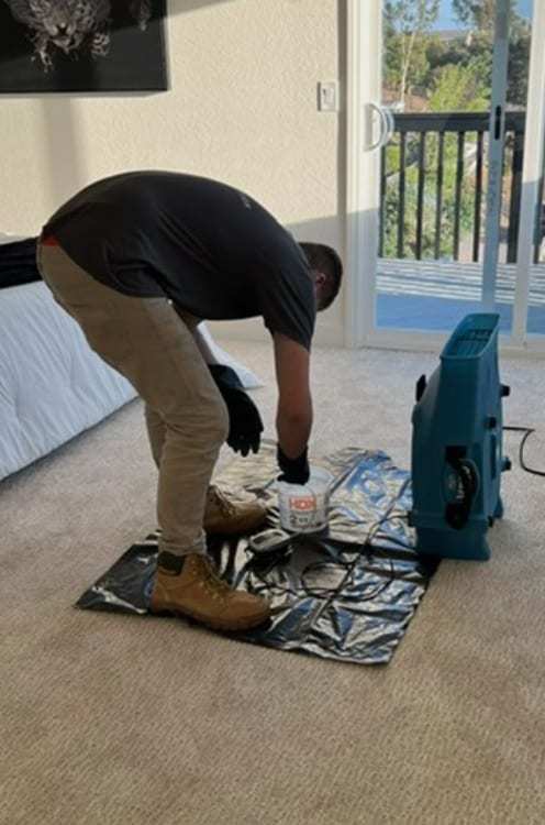 Technician setting an air mover on plastic sheeting in a bedroom