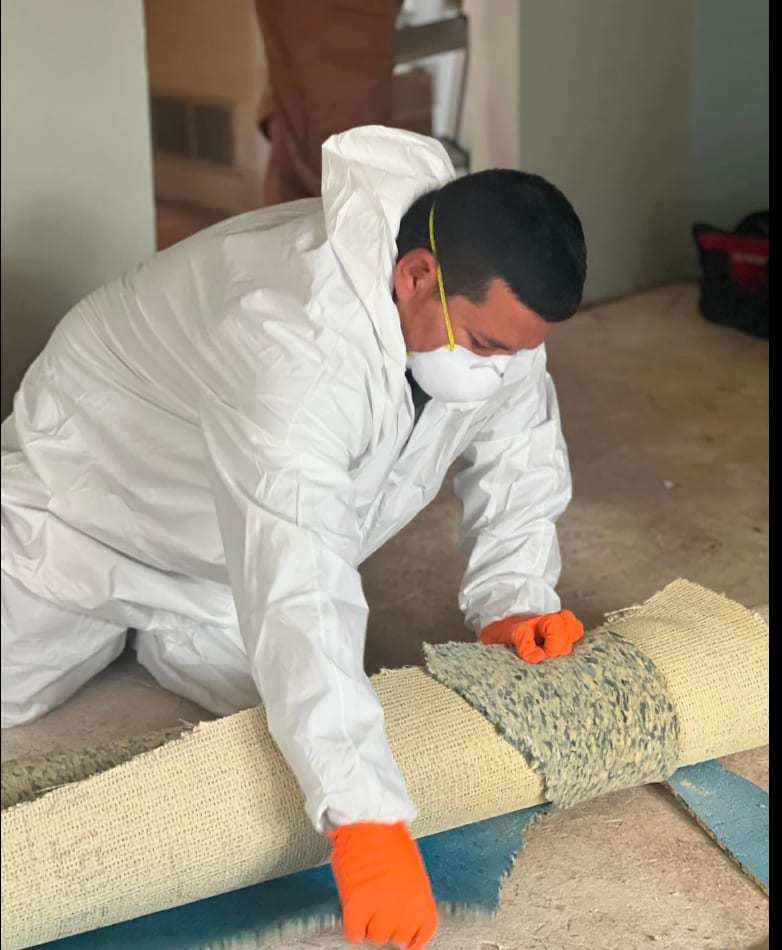 Technician in a protective suit rolling up wet carpet pad