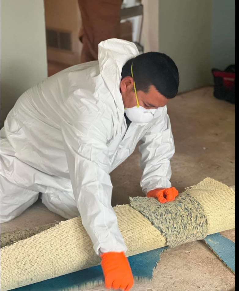 Technician in a protective suit rolling up wet carpet pad