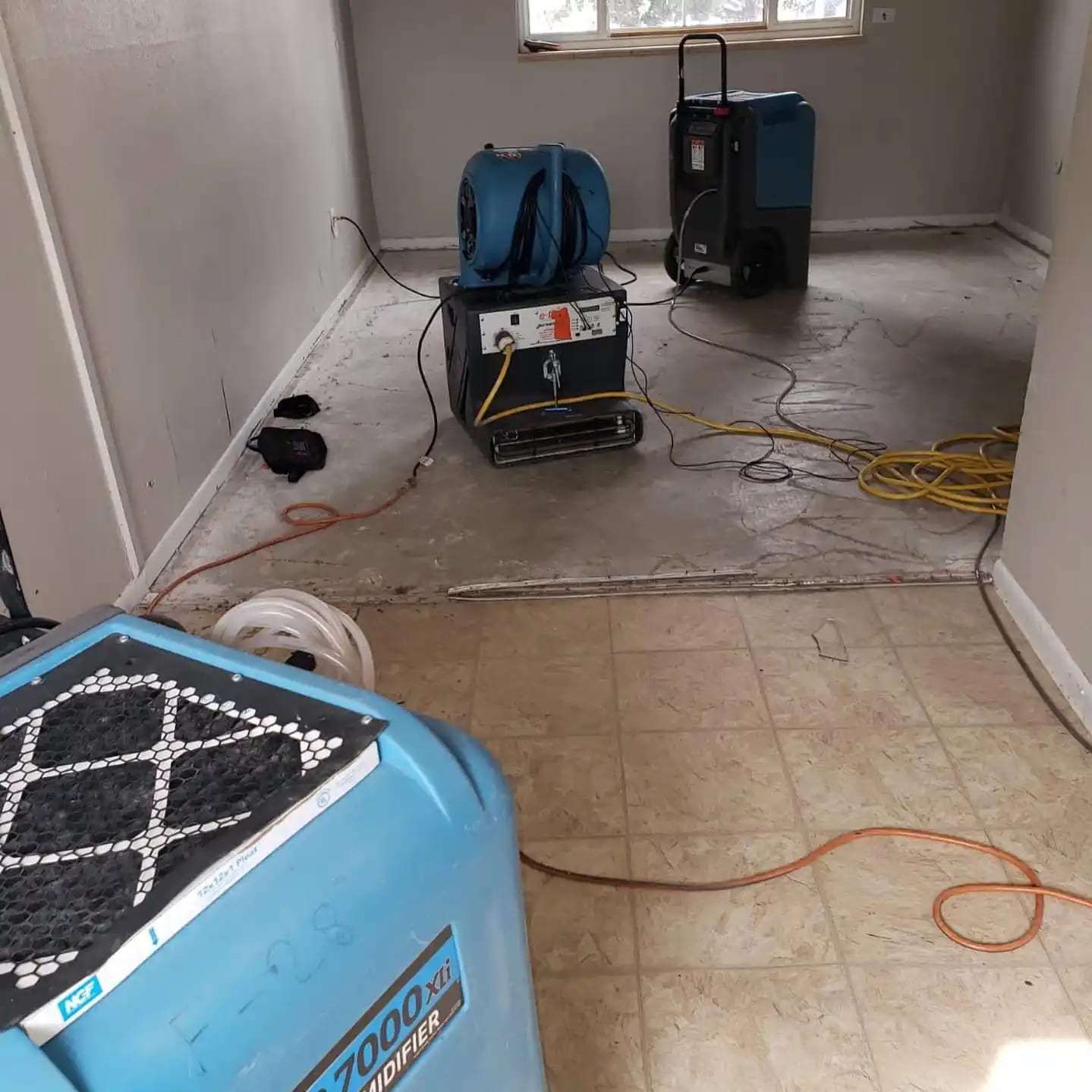 Basement room with the flooring removed, a dehumidifier and air movers drying