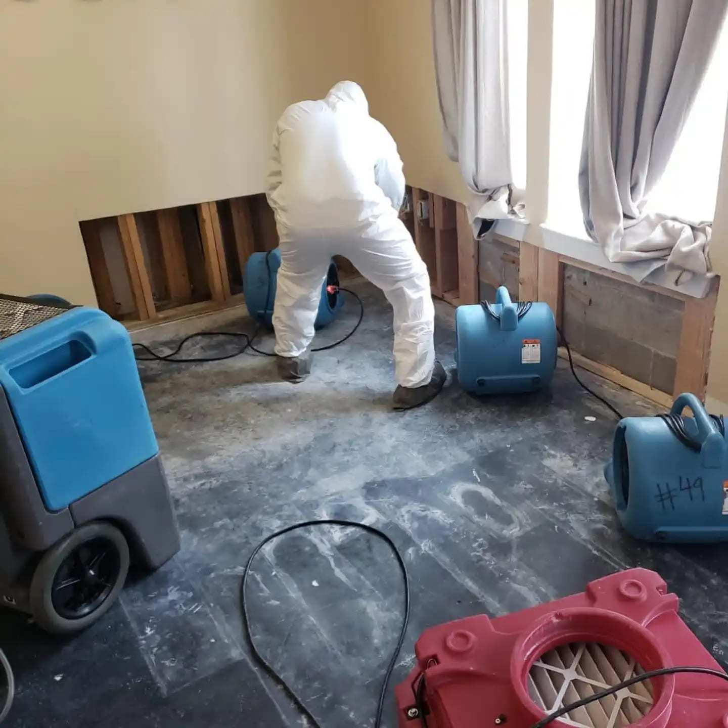 Technician checking flood-cut walls in a room with a dehumidifier and air movers