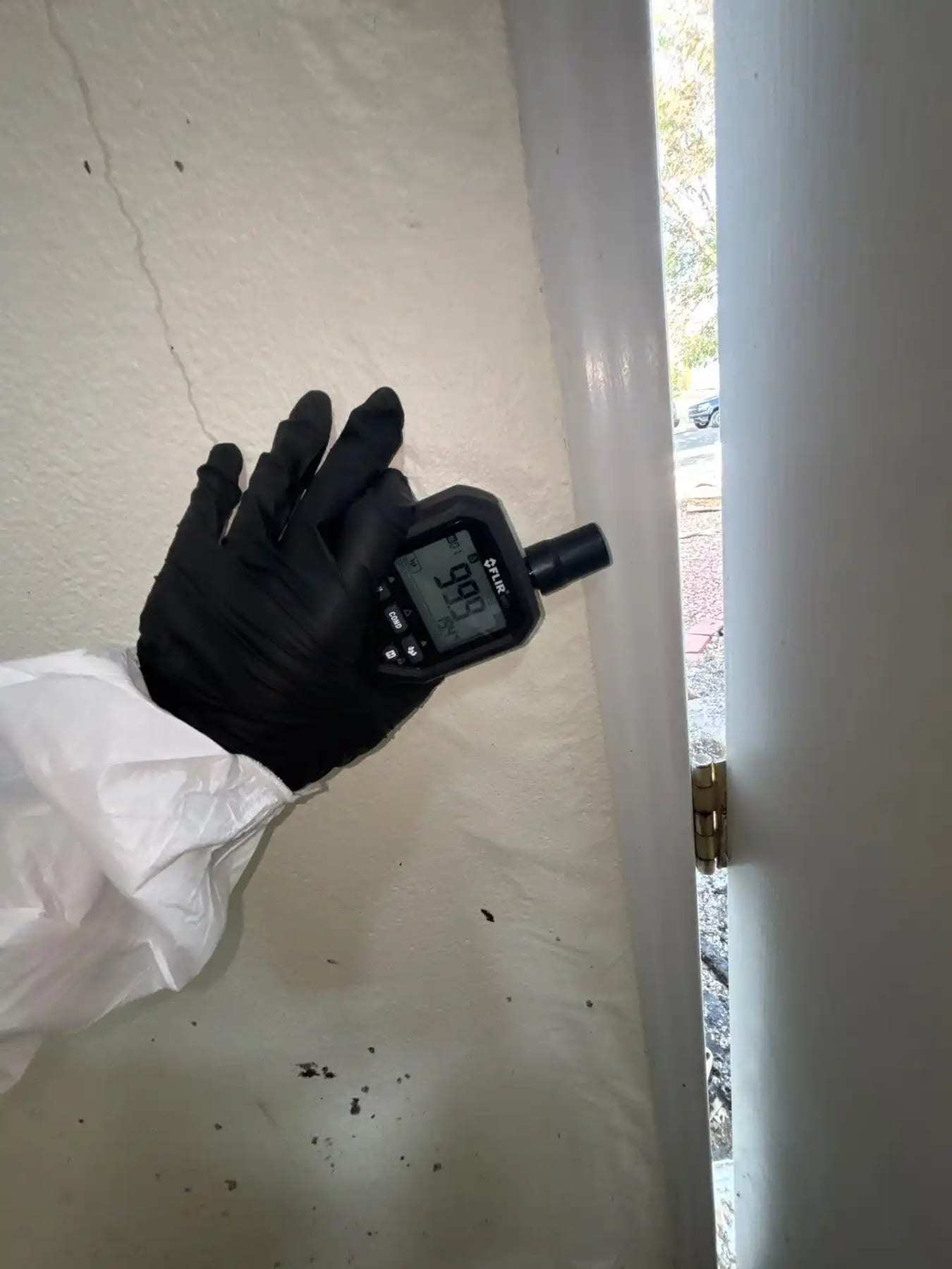 Gloved hand holding a moisture meter against a painted wall