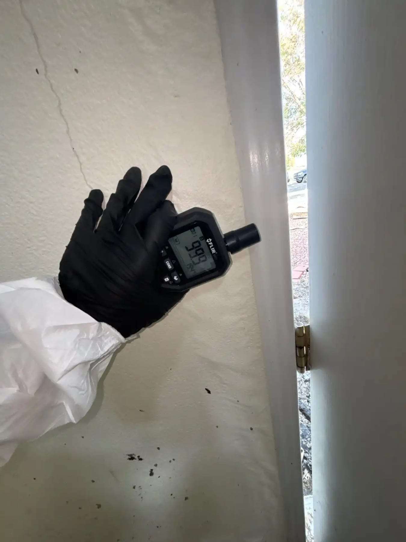 Gloved hand holding a moisture meter against a painted wall