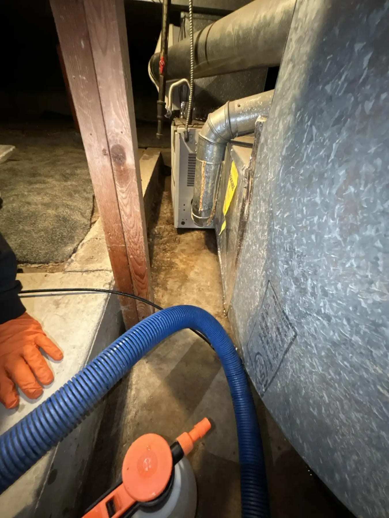 Drying hose connected to a dehumidifier beside a basement foundation wall