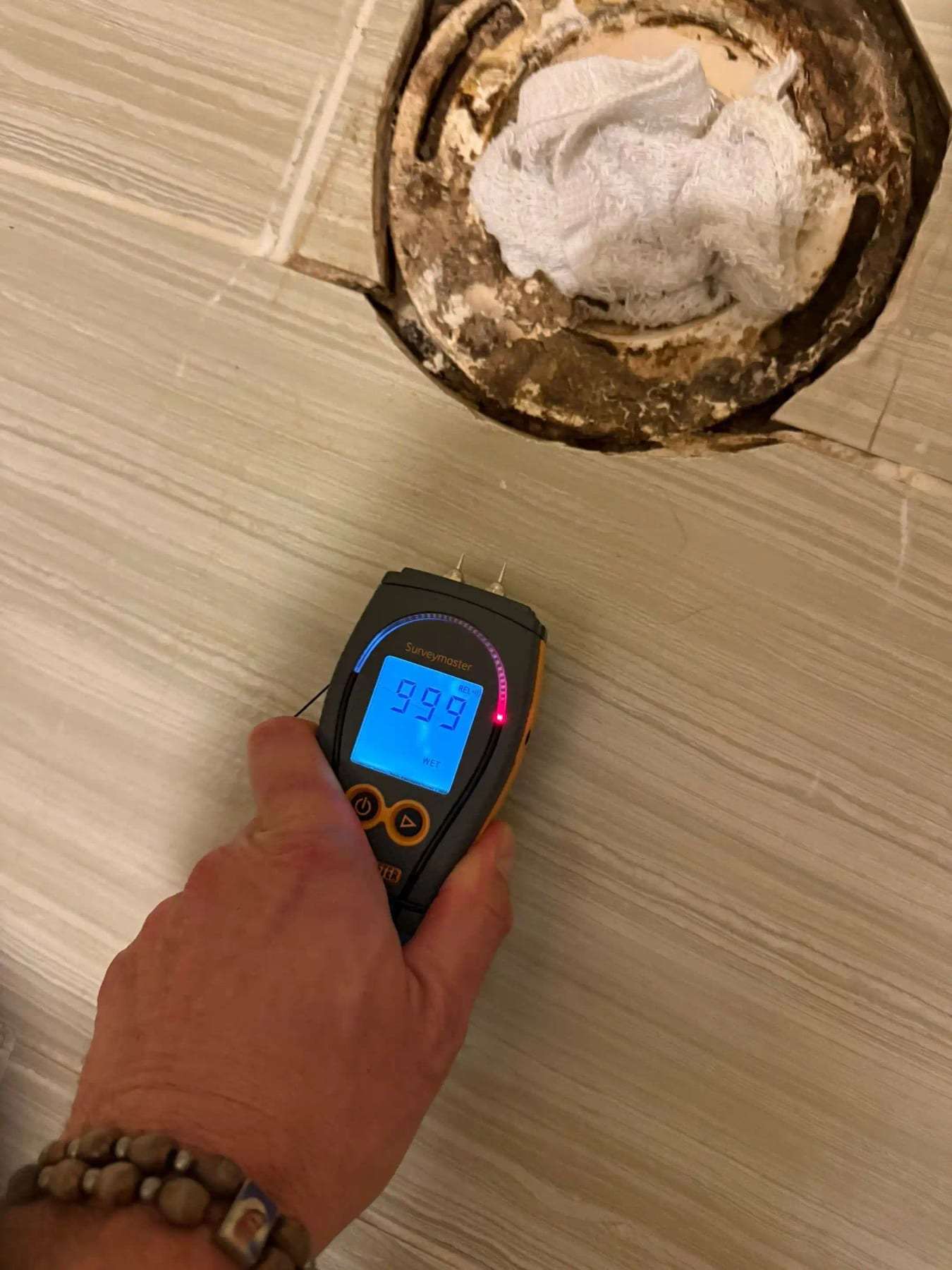 Moisture meter on tile beside a toilet flange with the toilet removed