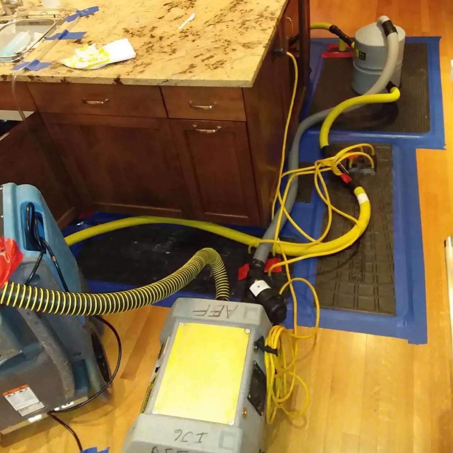Floor drying mats and hoses on a kitchen floor beside the cabinets