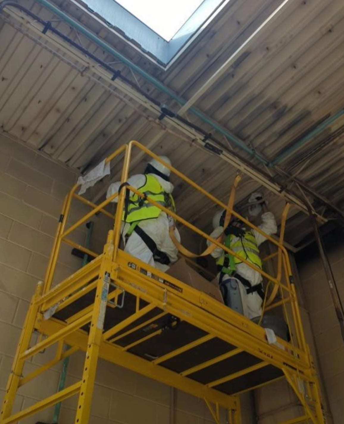 Technicians in protective suits on scaffolding cleaning a high ceiling