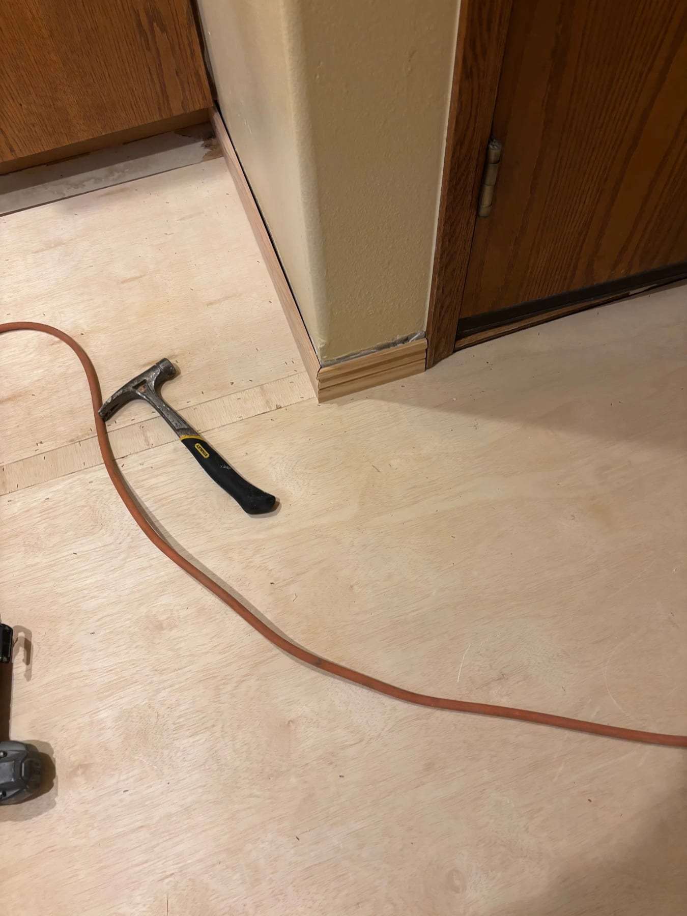 Hallway subfloor exposed with a hammer and a hose on the plywood