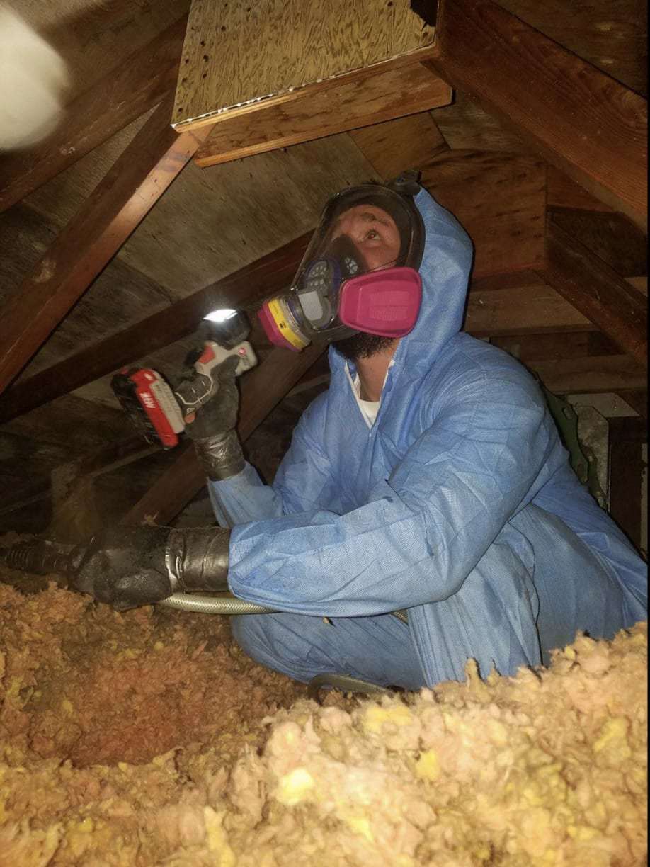 Technician in a respirator and protective suit in attic insulation