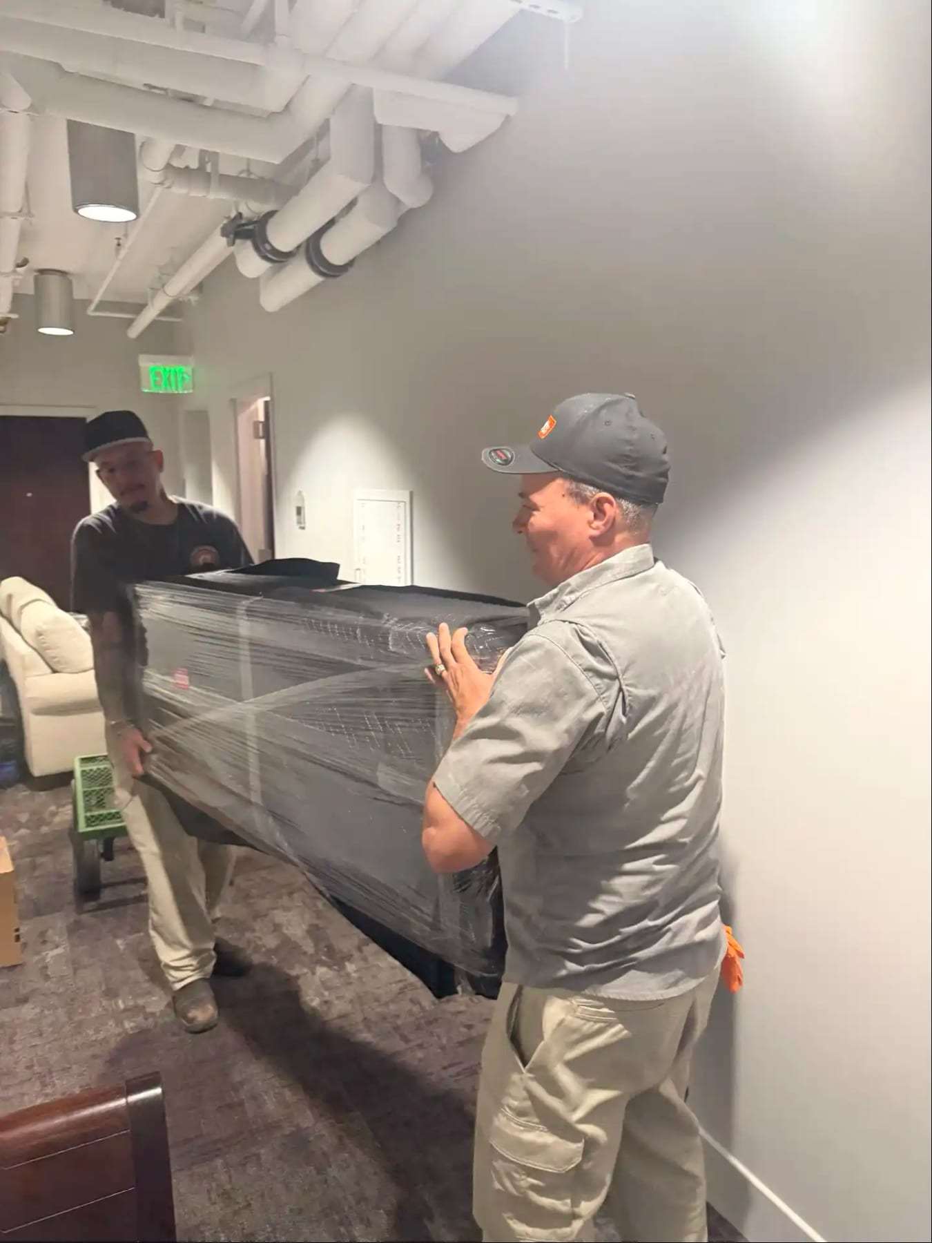 Two workers carrying a wrapped piece of furniture through an office