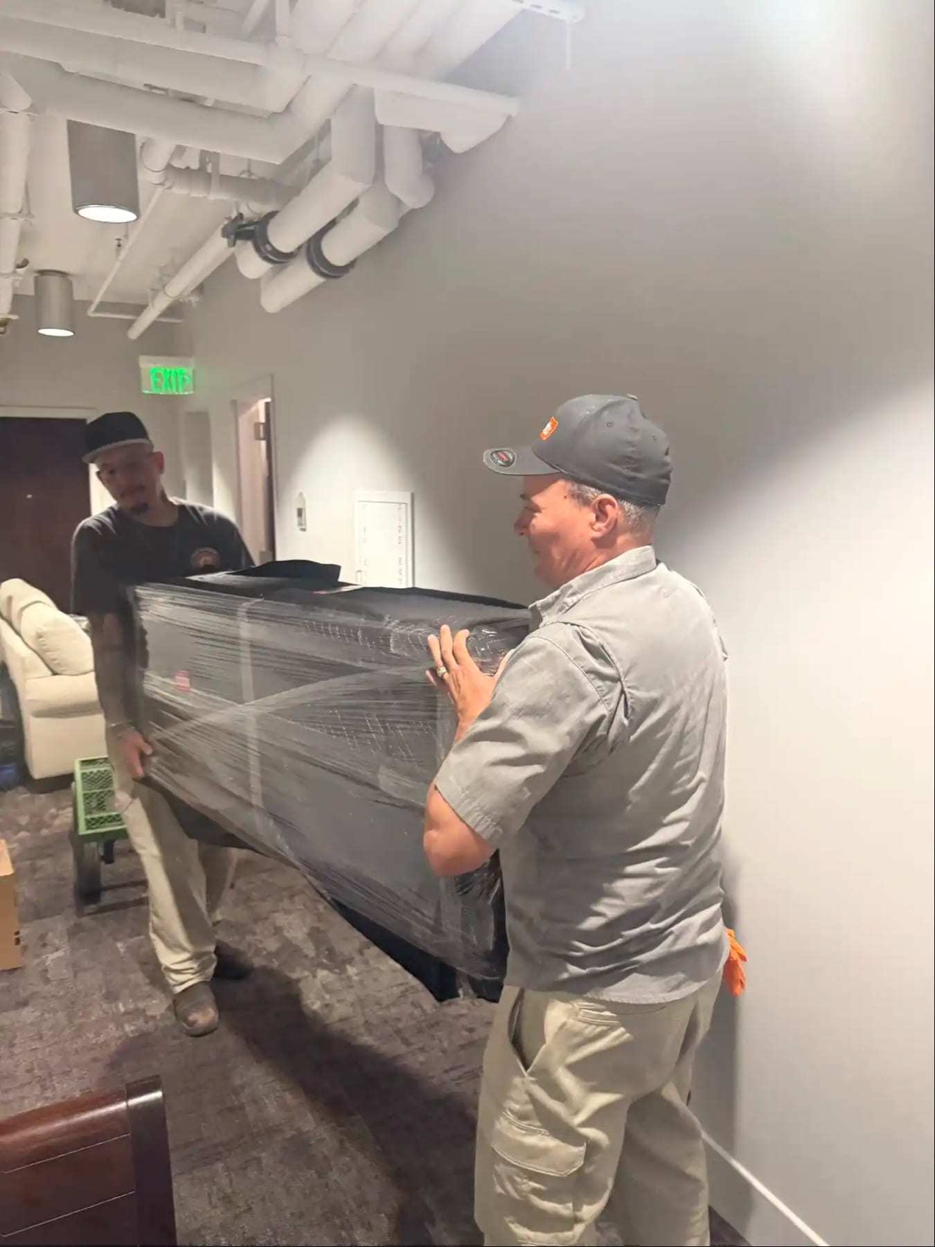Two workers carrying a wrapped piece of furniture through an office