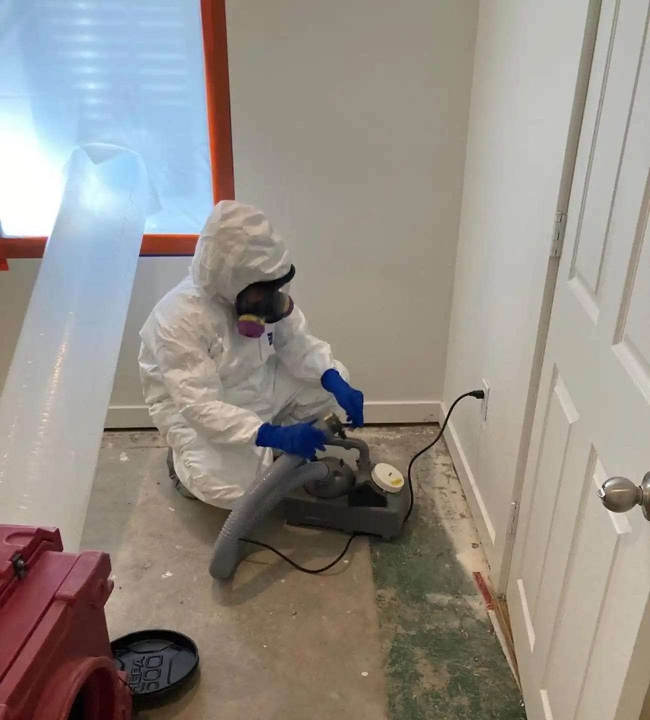 Technician in a protective suit and respirator cleaning the floor edge at a containment